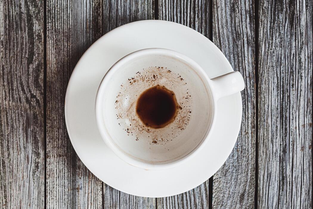 Two people sitting at a kitchen table, both looking slightly withdrawn, coffee cups between them